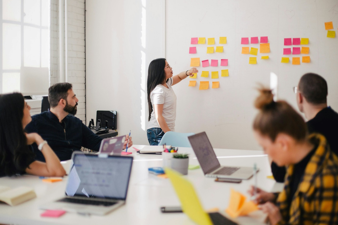 People in a meeting brainstorm with sticky notes on a whiteboard.